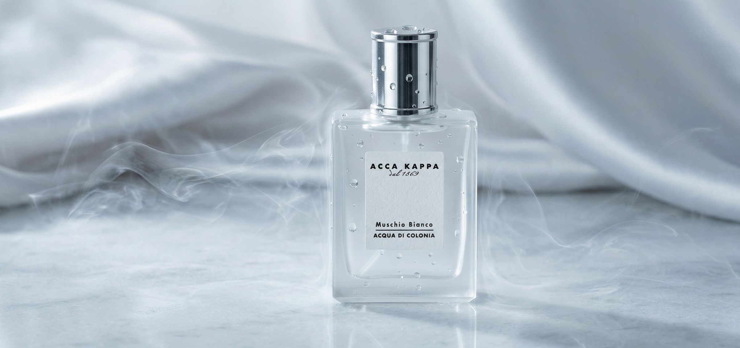 Perfume bottle with a silver cap and water droplets on a clear glass, labeled ACCA KAPPA Muschio Bianco Acqua di Colonia.