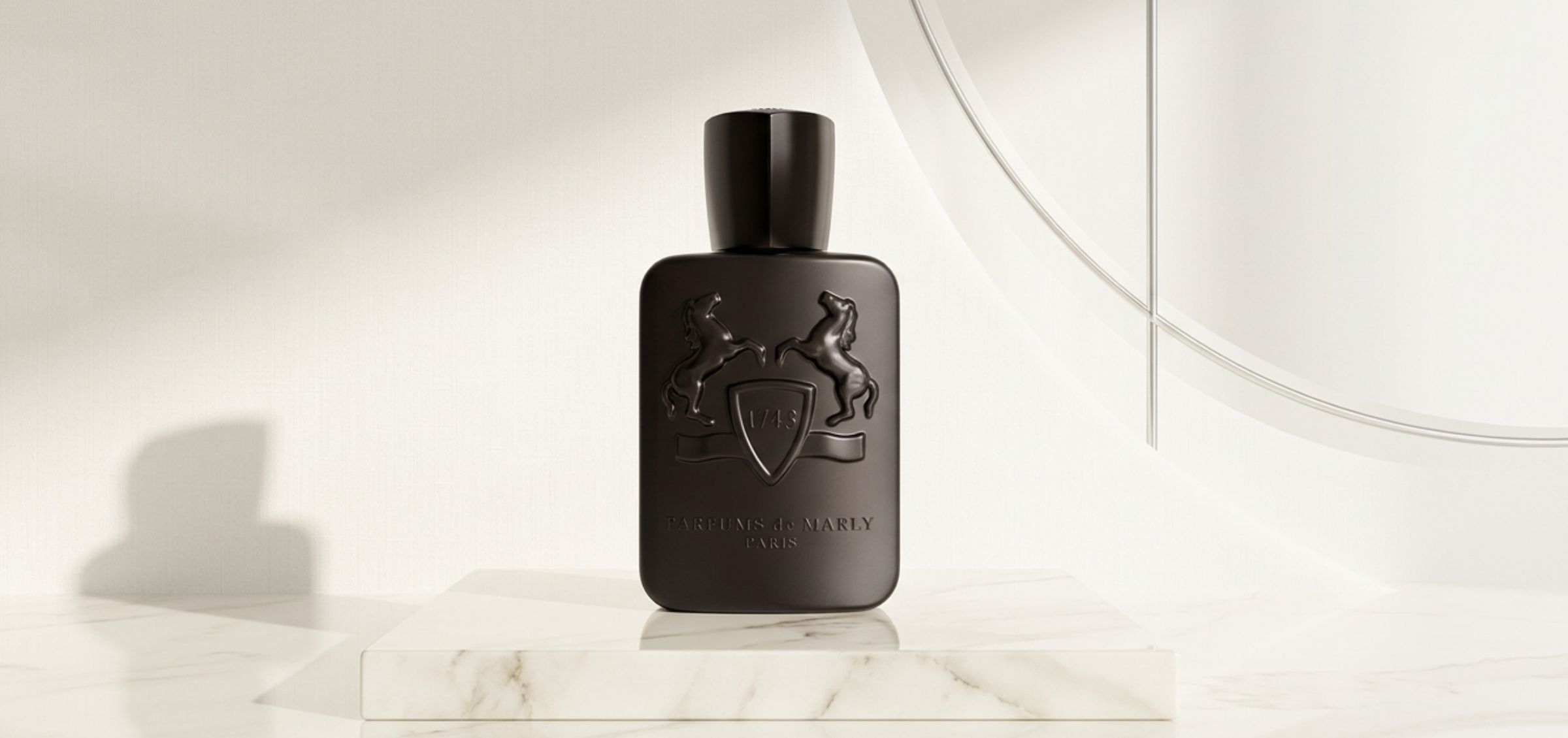 Dark rectangular perfume bottle with embossed horses and shield, on a white marble pedestal in a bright, minimalist display.