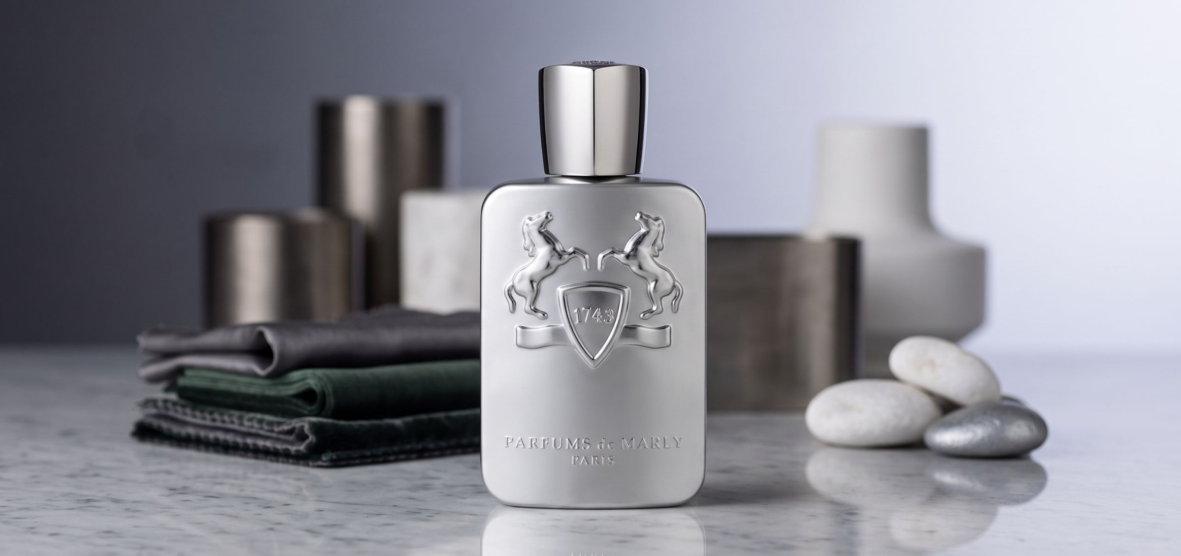Silver perfume bottle with an ornate crest and two rearing horses on the front, Parfums de Marly Paris, on a marble surface.