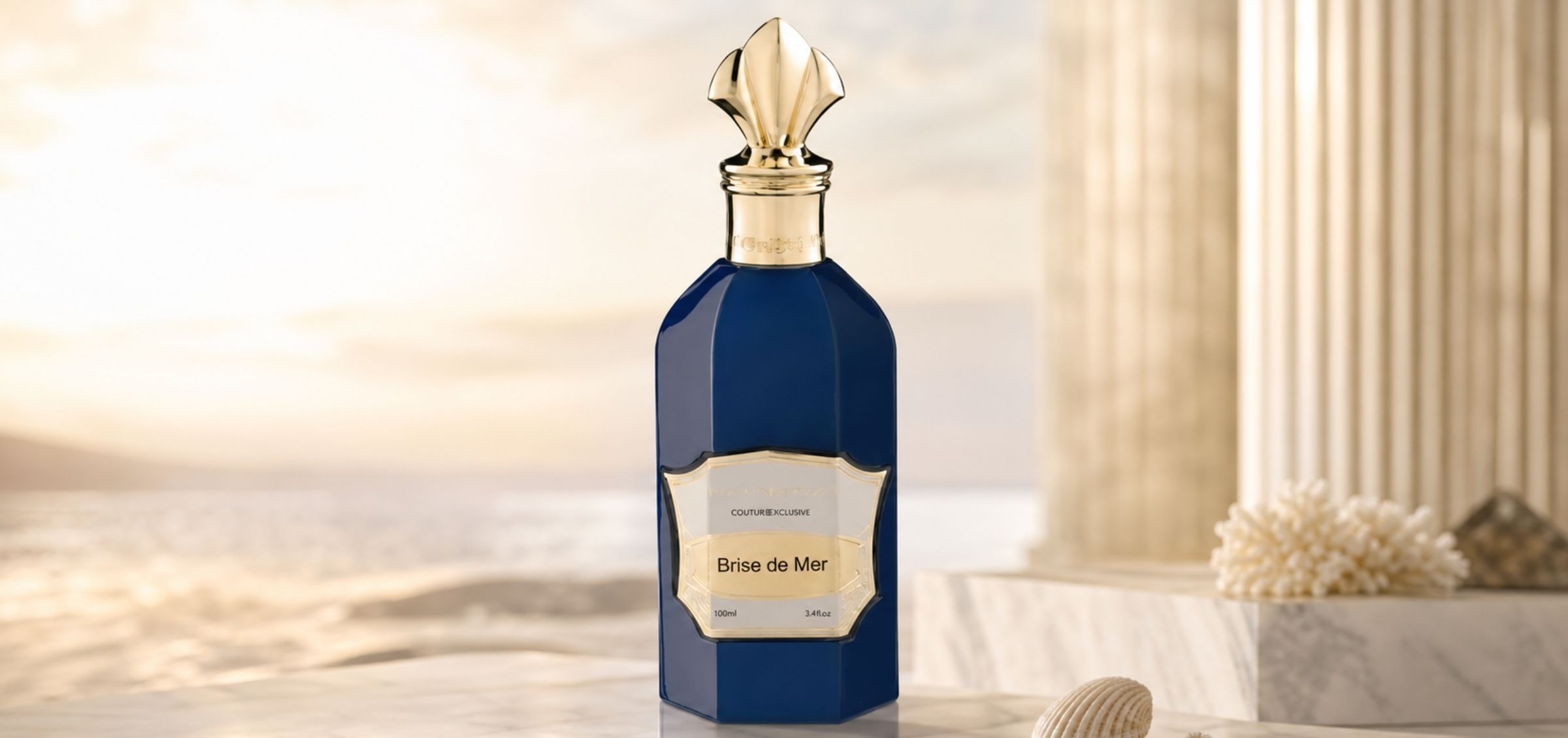 Blue glass perfume bottle with an ornate gold cap on a marble surface, label reads Brise de Mer, beach backdrop behind it.